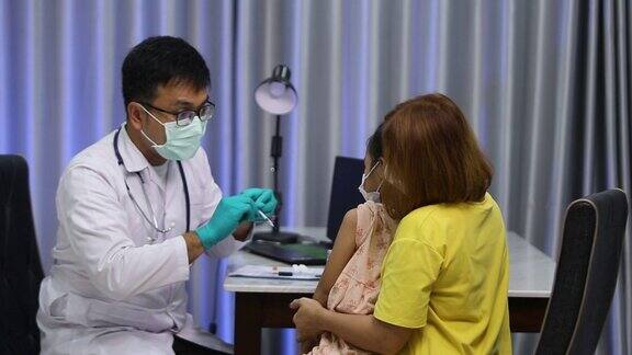 在儿童医院的儿科诊所带着口罩的亚洲男医生为亚洲女孩注射预防流感的疫苗母亲就在旁边注射治疗疾病引起儿童疼痛