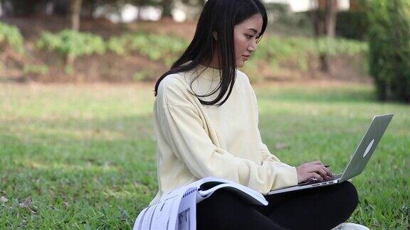 一群大学生亚洲人坐在绿色的草地上大笑一起在公园里工作和阅读