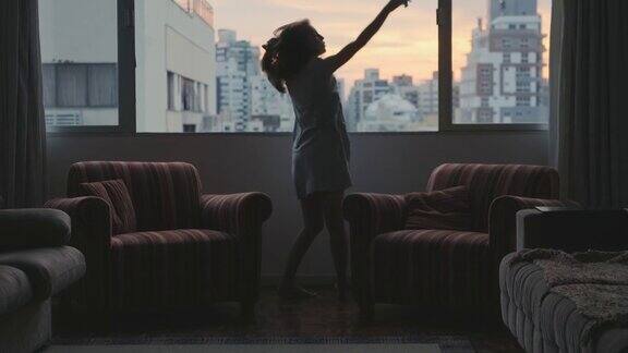 年轻女子独自在公寓的宽窗边跳舞