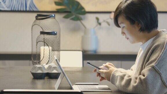 亚洲女性在家里使用笔记本电脑和智能手机
