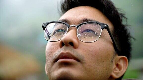 一名亚裔男子戴着眼镜将脸暴露在雨中