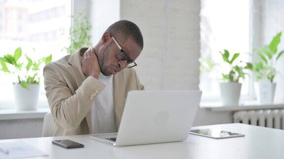 非洲男子在办公室使用笔记本电脑时颈部疼痛