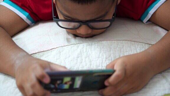 一个戴眼镜的男孩用智能手机玩游戏娱乐