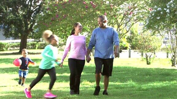 一家人在公园里父母手牵着手孩子们在跑步