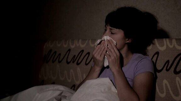 一个生病的女人晚上在家里的沙发上打喷嚏女孩流鼻涕拿纸巾流感症状医疗保健和医疗理念感冒是流感的感染