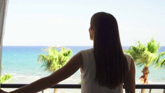 度假的女人拉开窗帘到阳台上欣赏地中海的海景