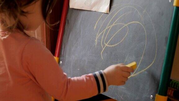 卷毛可爱的小女孩用蜡笔在黑板上画画