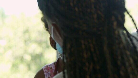 一个非洲家庭的母亲为她2岁的小女儿戴上医用口罩待在家里预防冠状病毒或Covid-19的流行面罩和面罩(非白种人)概念