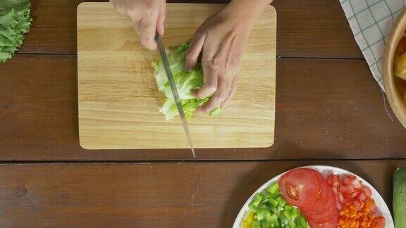 俯视图女首席制作沙拉健康食品和切生菜在切菜板上在厨房
