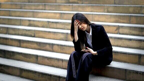 不开心的年轻女商人沮丧地坐在现代城市的楼梯上压力女性头痛并摸着头