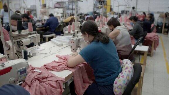 在一家服装厂的缝纫站工作的拉丁美洲妇女都戴着防护口罩