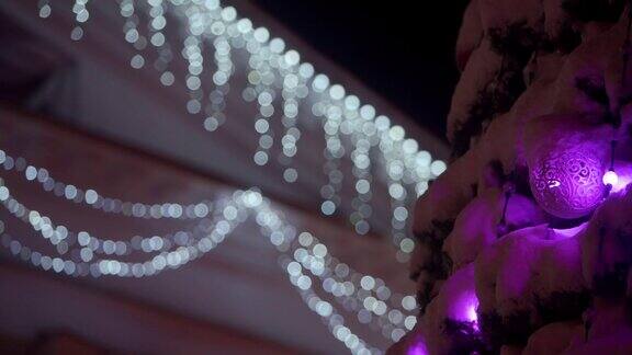 在下雪的冬夜城市广场上挂着发光的花环和装饰的大圣诞树特写镜头室外装饰的新年树缓慢的全景