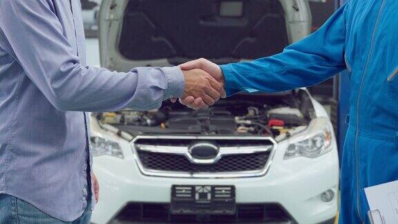 亚洲汽车修理工在车库里与客户握手汽车维修经理在机械车间工作为客户检查和维修汽车发动机后感到快乐和成功