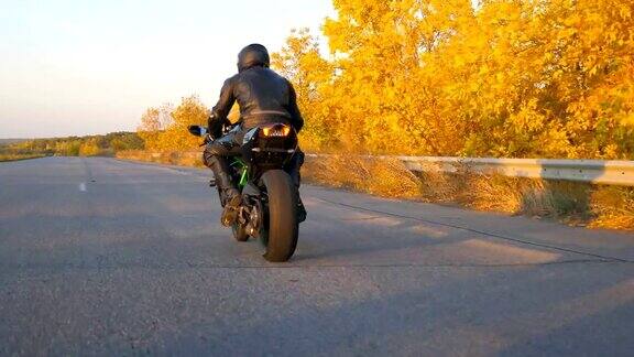 一个面目全非的男人在秋天的高速公路上骑着现代摩托车一名摩托车手在乡村公路上骑摩托车比赛在旅行中骑自行车的人自由和冒险后视