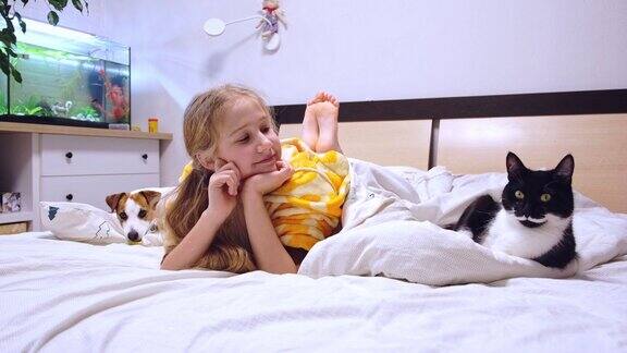 10-11岁的女孩躺在床上和宠物猫狗在一起微笑着看电视