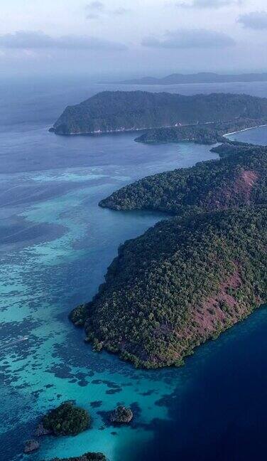 垂直视频的空中拍摄的热带岩石岛与蓝绿色的水和浅礁