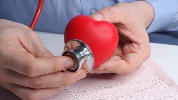心脏病专家医生检查一个玩具红心的心率耳内窥镜听诊器和心电图医疗保健和早期诊断