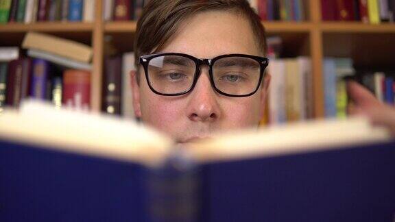 一个年轻人正在图书馆看书一个戴眼镜的人仔细地看这本书的特写背景是书架上的书图书馆的书
