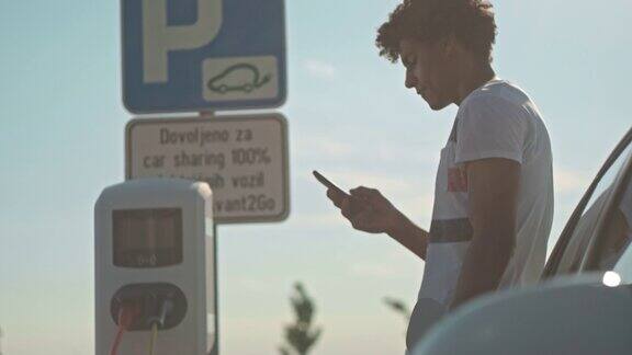 一名年轻人在停车场充电时使用智能手机