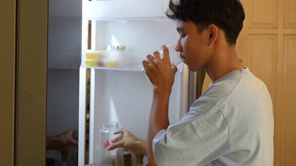 男子在打开的冰箱前喝水