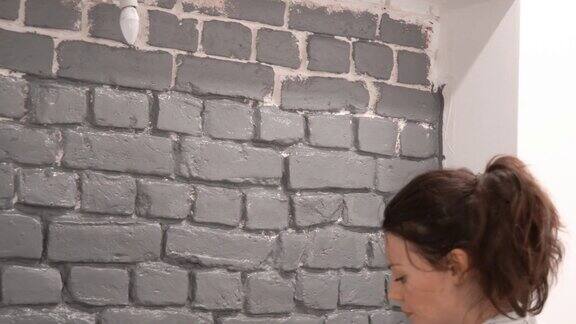 一个女孩用油漆滚筒在灰色的砖墙上作画的特写