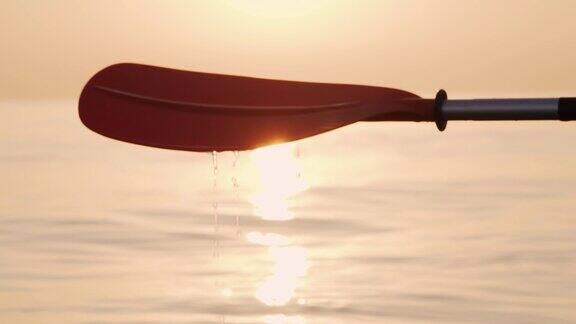 在平静的海面上橙色的皮艇划桨与美丽的慢动作运动员在金色日出的光线慢慢滴下的咸水