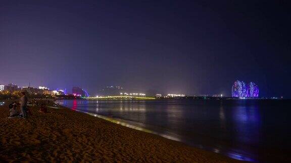 夜晚灯火辉煌的三亚拥挤的海滩著名的酒店全景4k时间推移海南岛中国