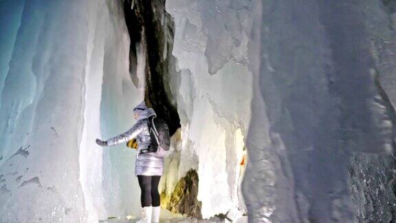 贝加尔湖冰洞上的女游客冬岛之旅女孩背包客正在冰洞中行走游客看着美丽的冰洞徒步旅行者穿银色夹克背包led灯