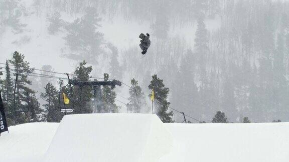 完成一个“前侧360Tucknee”技巧与森林和滑雪缆车在背景在科罗拉多州博尔德附近的埃尔多拉滑雪度假村在一个下雪的阴天从远处