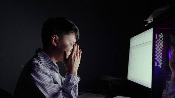 晚上一名亚洲男子在电脑前工作太久感到眼睛疲劳这是年轻人的生活方式