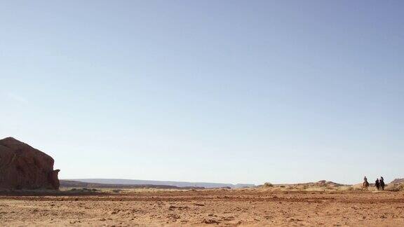 几个印第安人(纳瓦霍人)骑马通过纪念碑谷沙漠在亚利桑那州犹他州旁边的一个大的岩石在一个晴朗明亮的日子