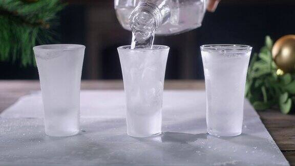 调酒师将伏特加从瓶子中倒入几个放在冰盘上的冷玻璃杯中