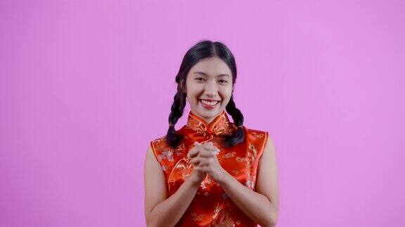 4K肖像梳着辫子的亚洲女孩穿着红色的中国民族服装(旗袍)双手握在一起说谢谢的手势蓝色背景的隔离室内工作室