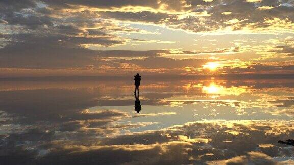 年轻的女摄影师在日落时漫步在盐湖上