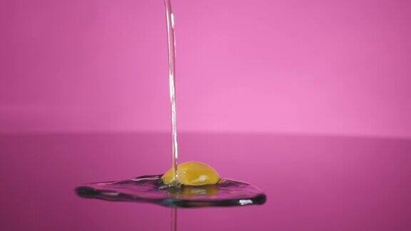 一个打碎的鸡蛋掉在粉红色背景上的桌子上