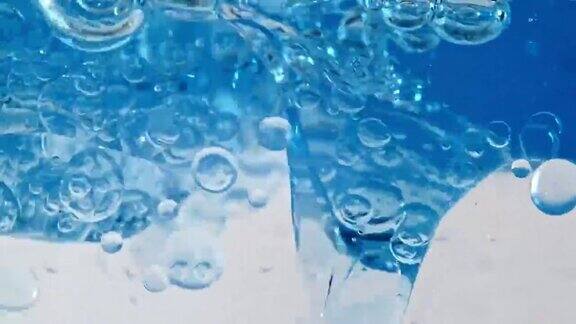 微距拍摄的各种气泡在水中上升在浅白色背景清澈的蓝色水中有气泡矿泉水富氧水慢动作