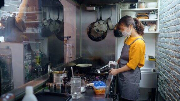 带防护口罩的女厨师在café和餐厅的商业厨房准备食物