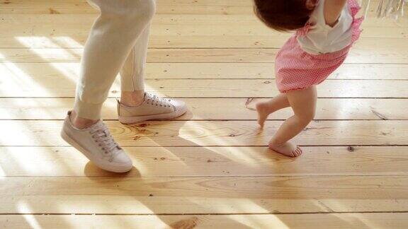一位陌生的母亲在慢镜头中帮助蹒跚学步的女儿在木地板上迈出第一步