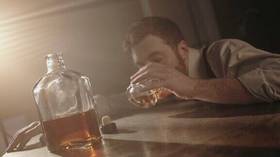 一个年轻的酒保喝得醉醺醺地睡在桌子上手里拿着一杯威士忌然后醒来喝了一小口又睡着了而摄像机把他放大和缩小