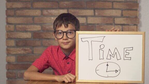 孩子坐在书桌前拿着写有时间的挂图背景是红砖墙上