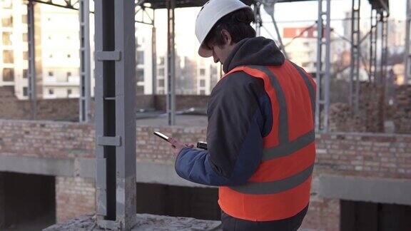 一名头戴白色头盔、手持智能手机的工头正在建筑工地工作建筑测量和建筑重建