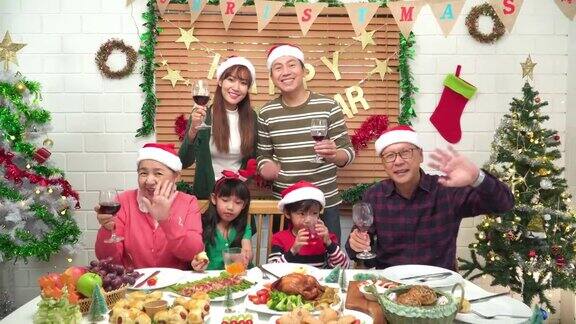 视频通话的时刻东南亚多代家庭微笑幸福围坐在可爱的餐桌上的食物晚餐一起欢呼庆祝12月的节日装饰的家