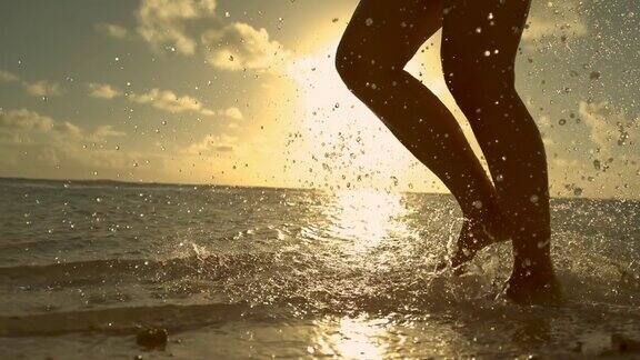 剪影:活泼的女孩在假日日出时在清新的海洋中奔跑