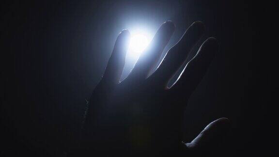 一个人的手伸向光手指玩弄着光并经过光源宗教、灵性和魔法概念