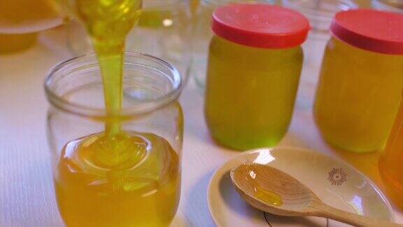一个女人把蜂蜜倒进白色桌子上的透明罐子里