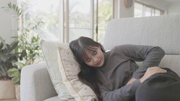年轻的亚洲女性躺在家里的沙发上肚子疼有肠道保健