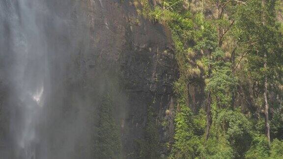 瀑布在岩石悬崖与绿色的树木和草缓慢