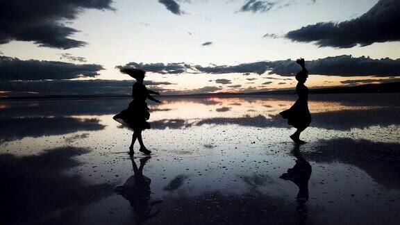 两个年轻漂亮的芭蕾舞演员在盐湖上跳舞日落时分芭蕾舞演员在水面上跳舞