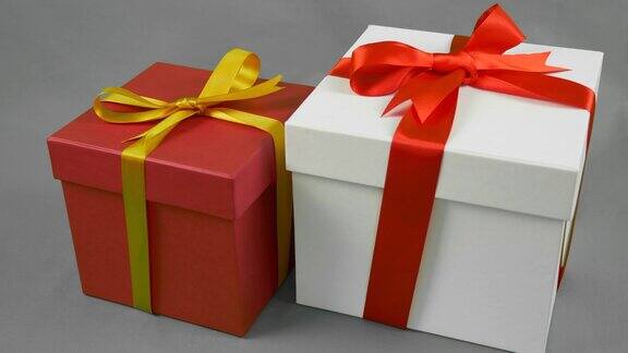 灰色背景下的两个礼品盒白色礼盒与红色丝带蝴蝶结和红色礼盒与金黄色蝴蝶结支架