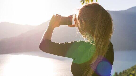 女人在日落时拍摄湖面上的山脉